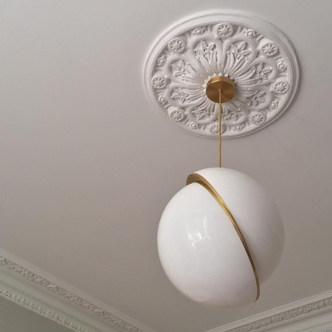 Close view of a Clérachic pendant hanging from an ornate white ceiling rose with a brass canopy.