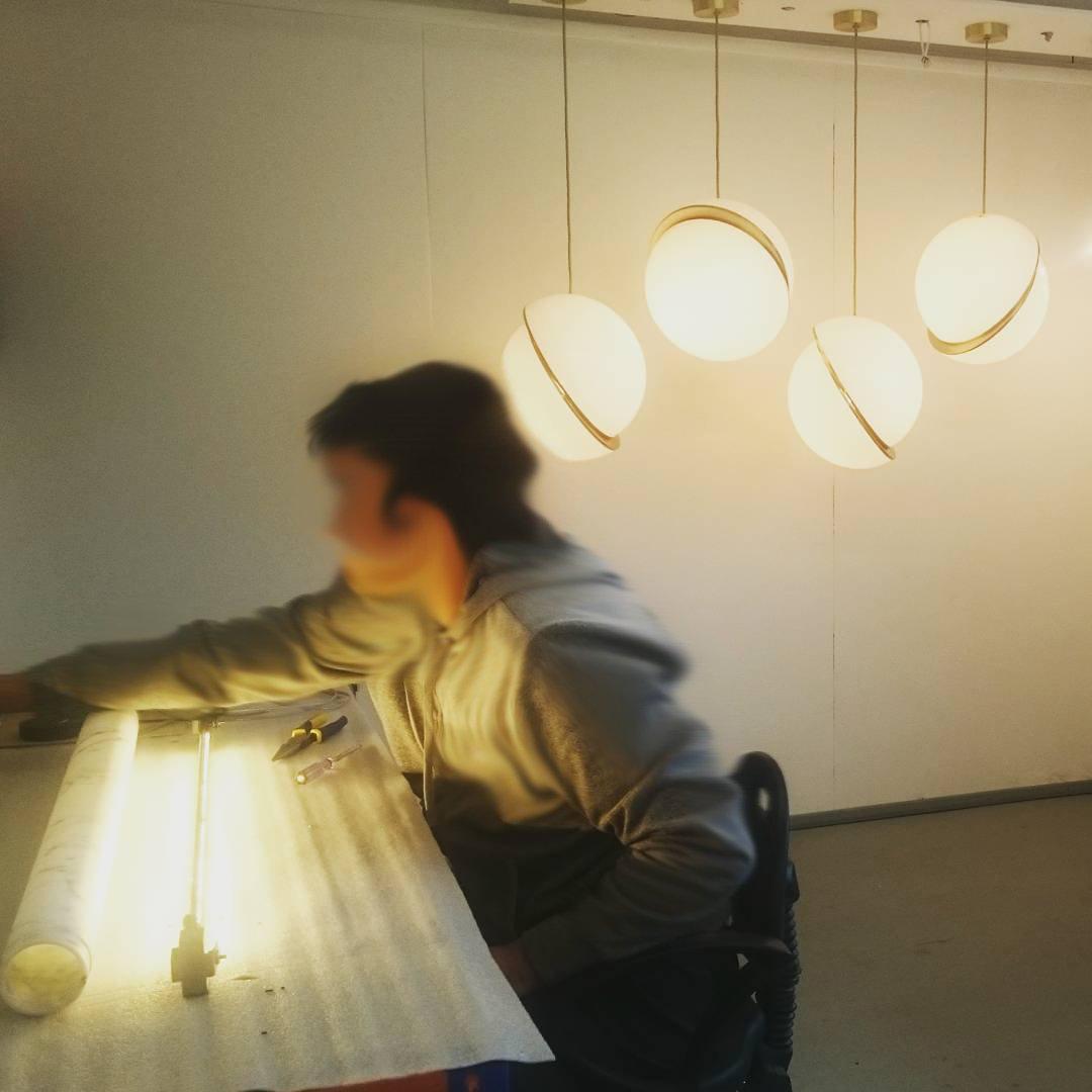 Low over a lit work table, four brass-crescent pendants of this Clérachic fixture catch the glow.