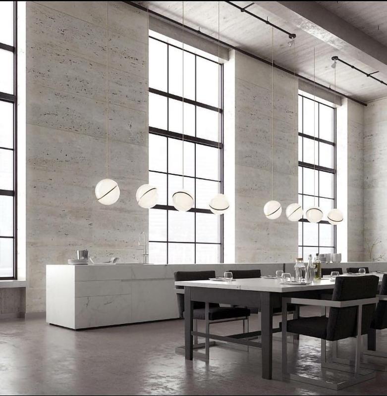Beside tall factory-style windows, a row of Clérachic pendants steps down above a stone dining table.
