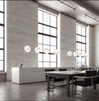 Beside tall factory-style windows, a row of Clérachic pendants steps down above a stone dining table.