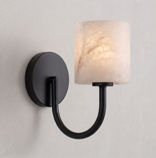 This Clérachic wall sconce in matte black casts a warm glow through its cylindrical alabaster shade.