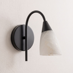 Set against a plain wall, the matte black arm of this Clérachic sconce curves up to its alabaster shade.