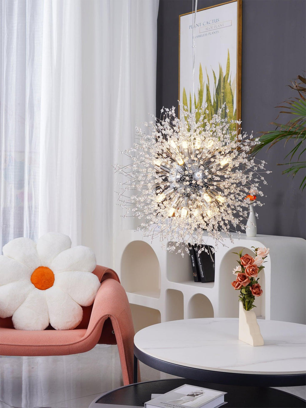A pink accent chair and an orange daisy pillow sit beneath this Clérachic chandelier near a small round table.