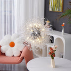 A pink accent chair with a white daisy pillow sits beneath this Clérachic chandelier near a marble-topped table.