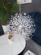 A potted plant and a dried flower arrangement sit near this Clérachic chandelier beside the edge of a navy sofa.