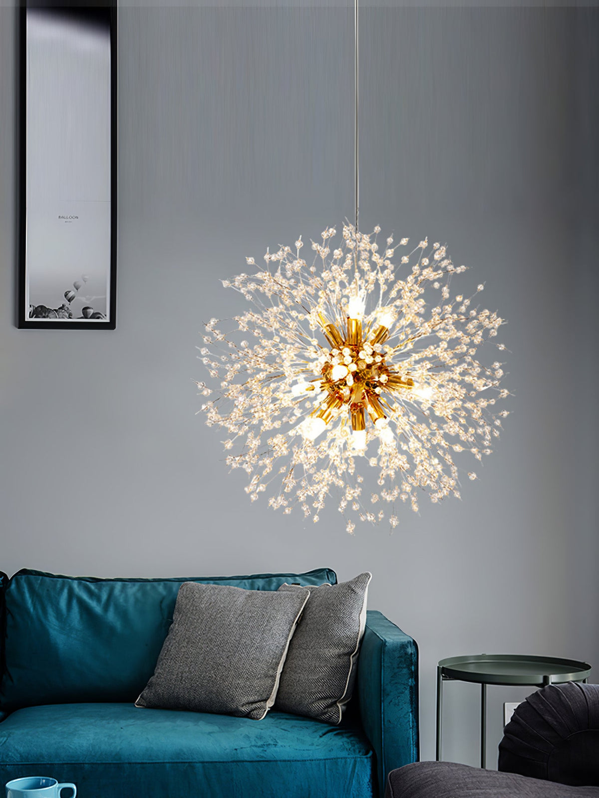 This Clérachic chandelier hangs lit beside a grey sofa with cushions and a framed print on the wall.