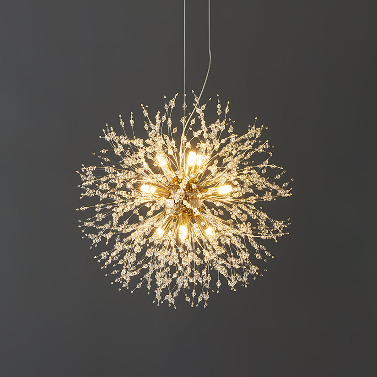 This Clérachic chandelier hangs lit against a dark charcoal wall, its crystal-tipped branches glowing warmly.