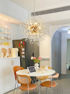 Another view of this Clérachic chandelier lit above a round dining nook with open shelving and a stainless fridge.
