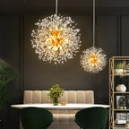 Two of this Clérachic chandelier hang at different heights above a dark-panelled dining room with green upholstered chairs.