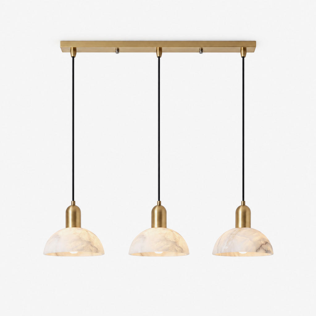 Photographed in brushed brass against white, this Clérachic pendant lines up three alabaster dome shades.