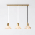 Seen in full against white, this brass Clérachic pendant fans three alabaster domes from a linear bar.