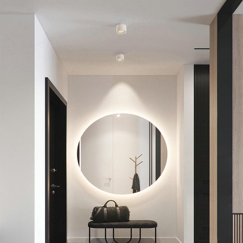 This Clérachic downlight in white is mounted in a hallway near a backlit round mirror and a black entry table.