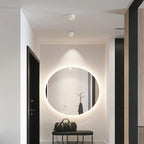 This Clérachic downlight in white is mounted in a hallway near a backlit round mirror and a black entry table.