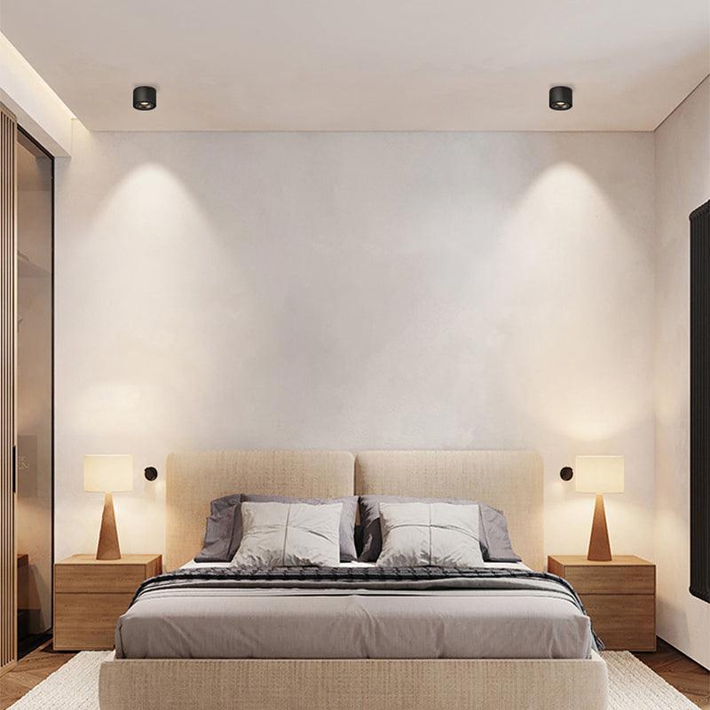 Two black units of this Clérachic downlight light a bedroom wall above a wood-framed bed and matching nightstand lamps.