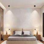 Two black units of this Clérachic downlight light a bedroom wall above a wood-framed bed and matching nightstand lamps.