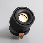 Close view of this Clérachic downlight in black, angled sharply, its lens rimmed with a thin amber ring and clips extended.