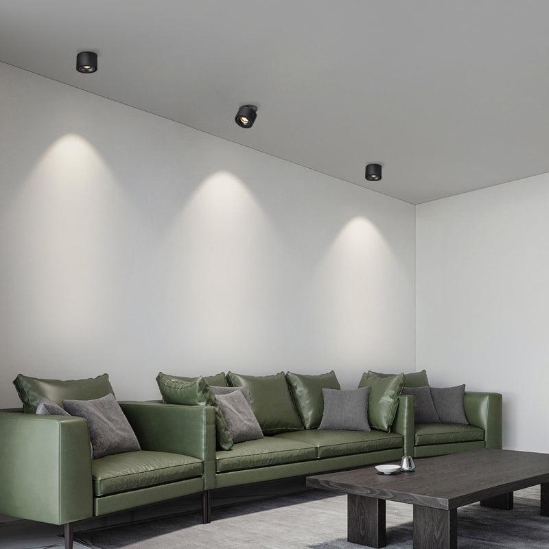 Three black units of this Clérachic downlight line a living room ceiling above a dark green leather sofa.