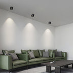 Three black units of this Clérachic downlight line a living room ceiling above a dark green leather sofa.