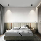 Black units of this Clérachic downlight wash warm light down a panelled green headboard wall in a bedroom.