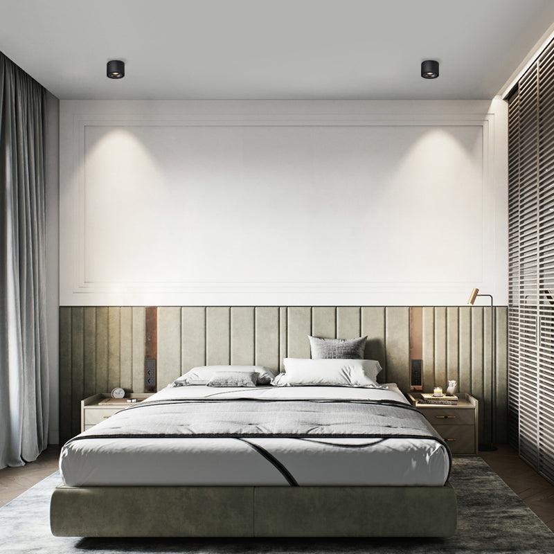 Black units of this Clérachic downlight wash warm light down a panelled green headboard wall in a bedroom.