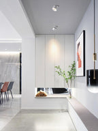 White units of this Clérachic downlight line a hallway ceiling near framed art, a pendant and a built-in bench.