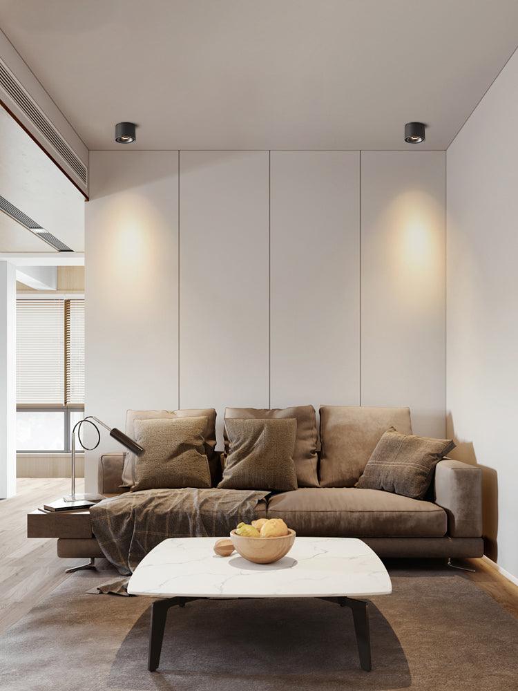 Two black units of this Clérachic downlight light a panelled wall above a brown sofa and marble coffee table.