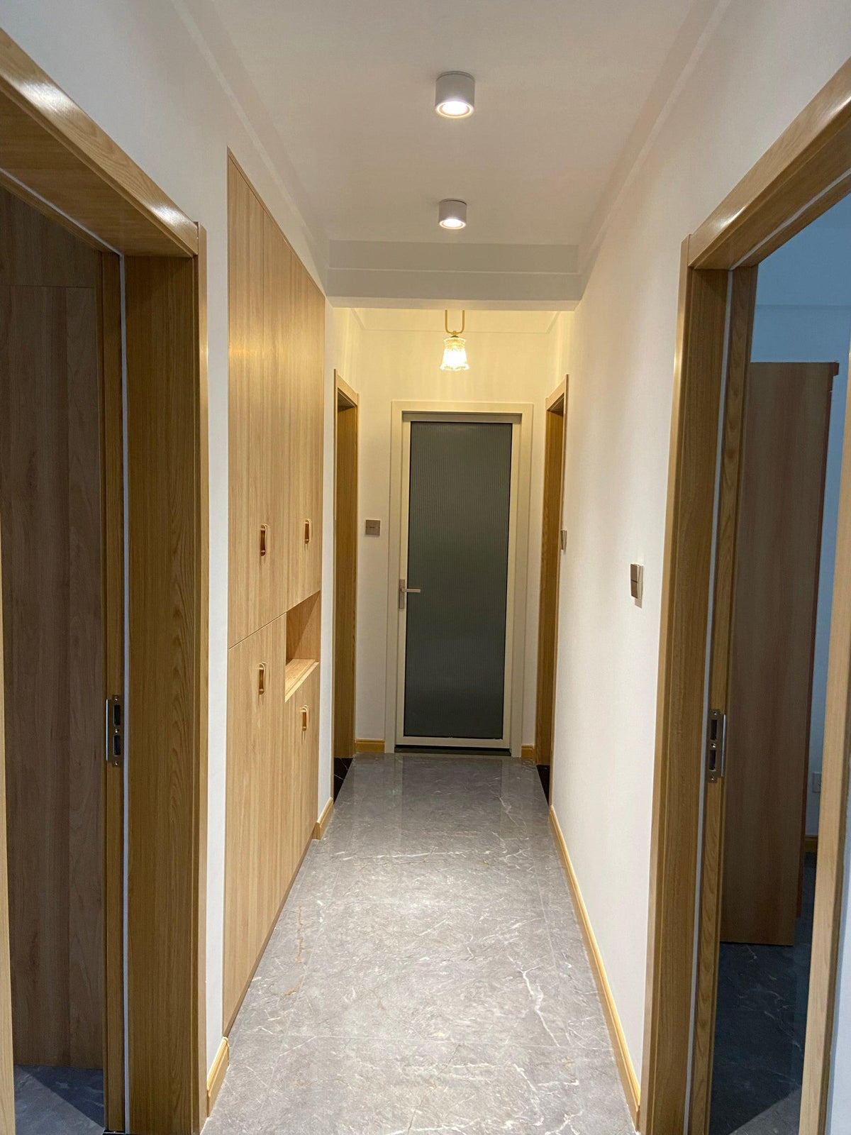 A single black unit of this Clérachic downlight lights a hallway lined with wood-panel doors and stone flooring.