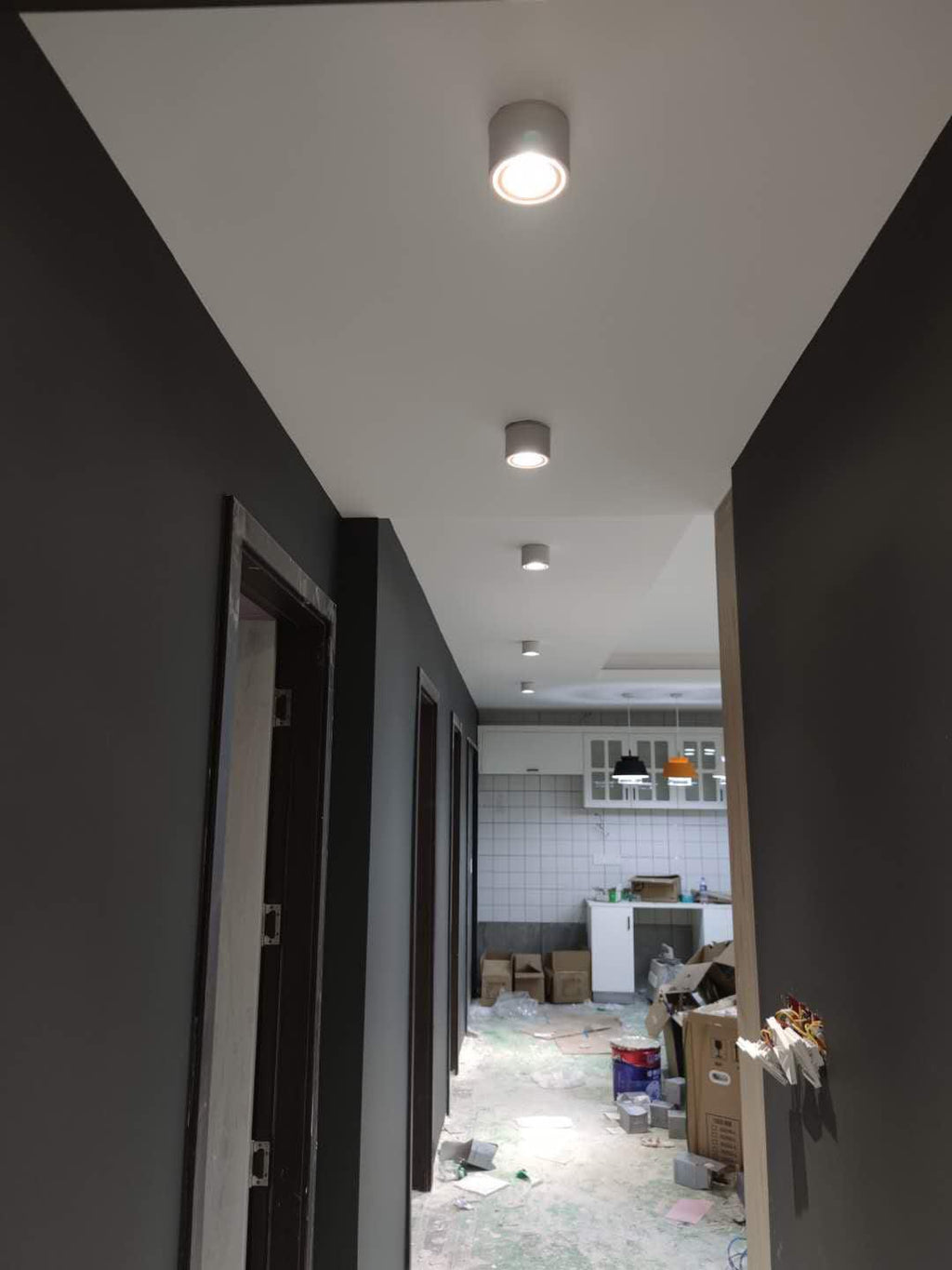 Black units of this Clérachic downlight line a dark hallway ceiling, spaced along its length toward a lit doorway.