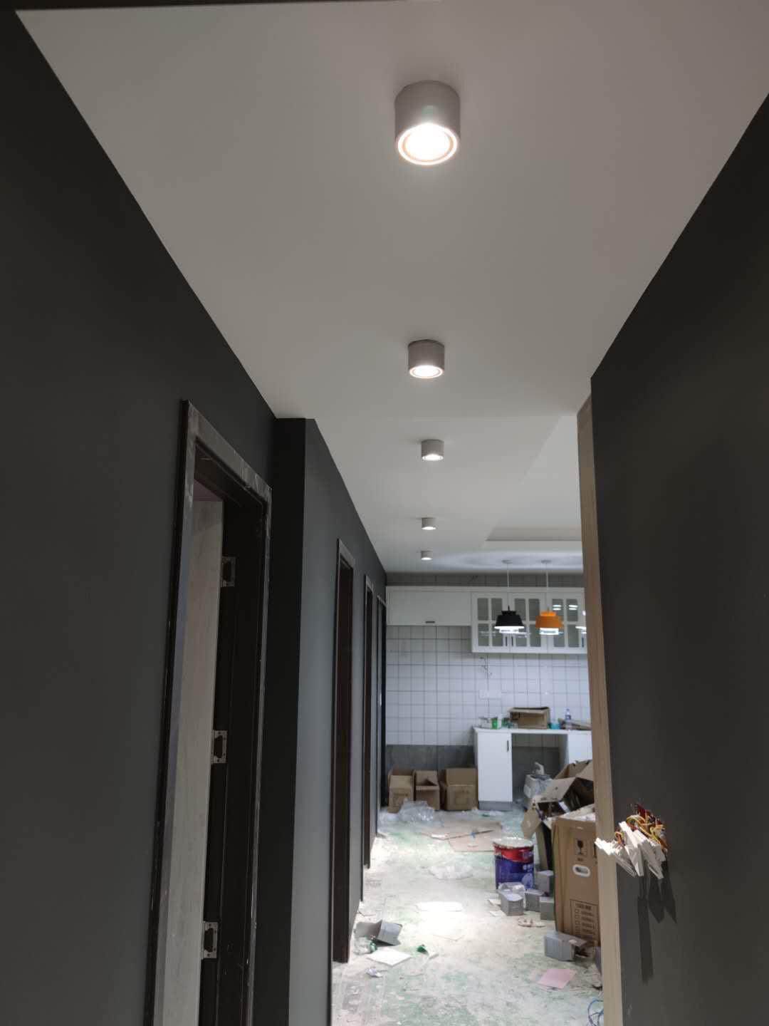 Black units of this Clérachic downlight line a dark hallway ceiling, spaced along its length toward a lit doorway.