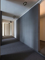 Black units of this Clérachic downlight line a corridor ceiling past dark tiled walls and a patterned screen door.