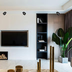 Angled black units of this Clérachic downlight line a living room ceiling above open wood shelving and a television.