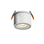 Close view of this Clérachic downlight in white, spring clips extended, lens lit with its amber ring, on a plain backdrop.