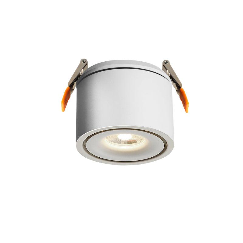 Close view of this Clérachic downlight in white, spring clips extended, lens lit with its amber ring, on a plain backdrop.