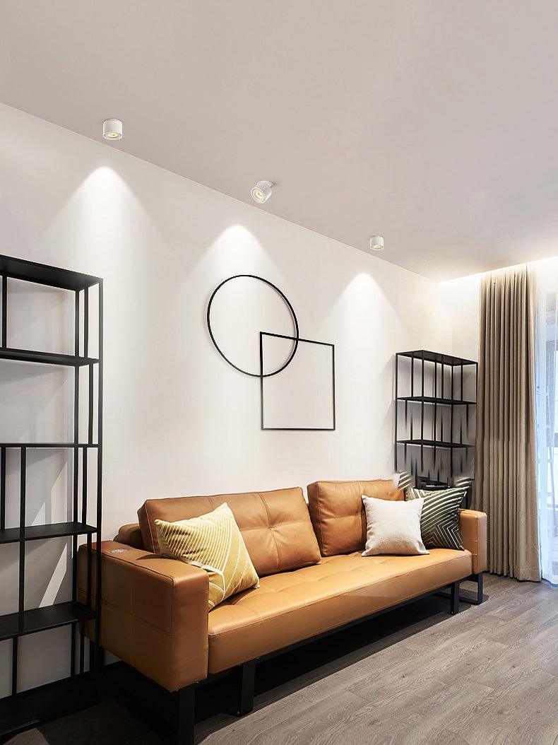 White units of this Clérachic downlight light a living room with a tan leather sofa and circular wall art.