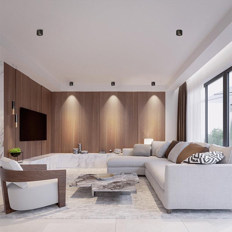 Black units of this Clérachic downlight line a living room ceiling above a wood-panelled media wall and sectional sofa.