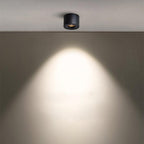 This Clérachic downlight in black projects a wide, warm cone of light down a plain beige wall.