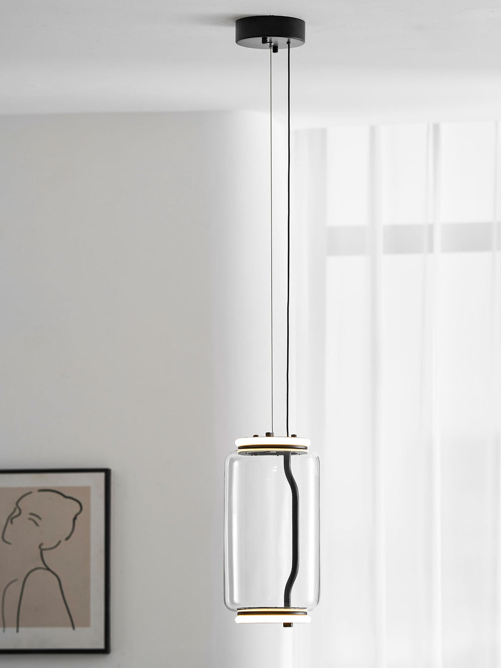 A single wide-cylinder Clérachic pendant hangs in a white room beside a line-drawn portrait print.
