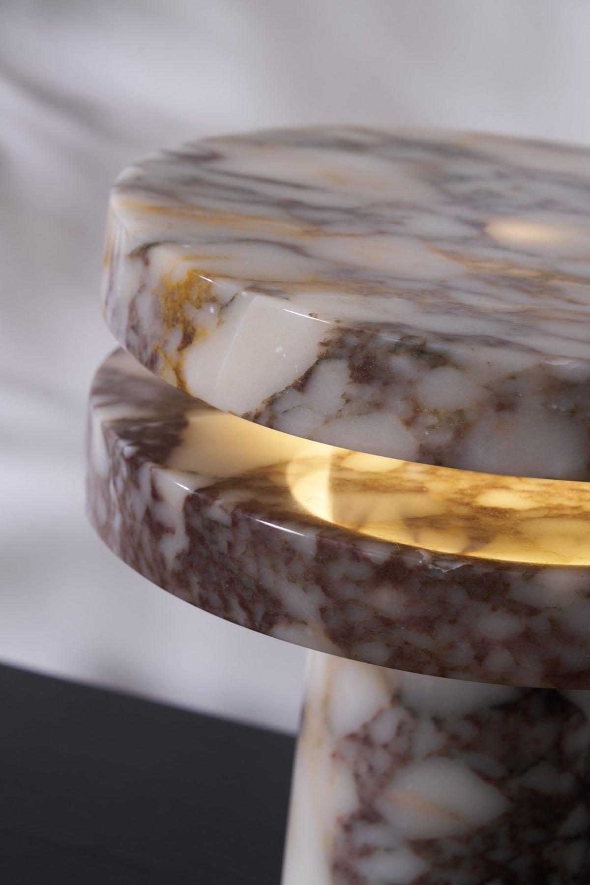 Macro crop of the Clérachic lamp's disc gap, the LED glow lighting the veined marble from underneath at an angle.
