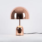 This Clérachic rose gold table lamp stands against a plain backdrop, its black cord trailing to one side.