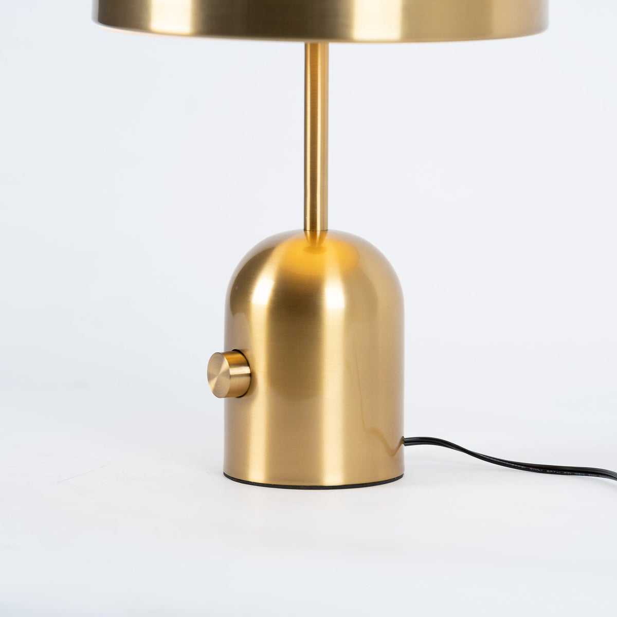 A close-up of the brushed gold base and switch dial on this Clérachic table lamp, with its cord visible below.