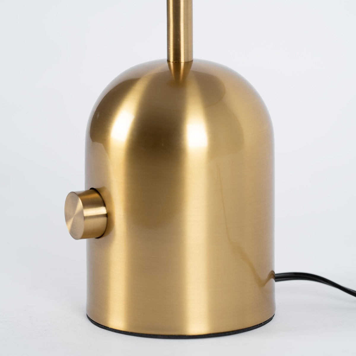 A close-up shows the large knob switch on the brushed gold base of this Clérachic table lamp, cord trailing right.