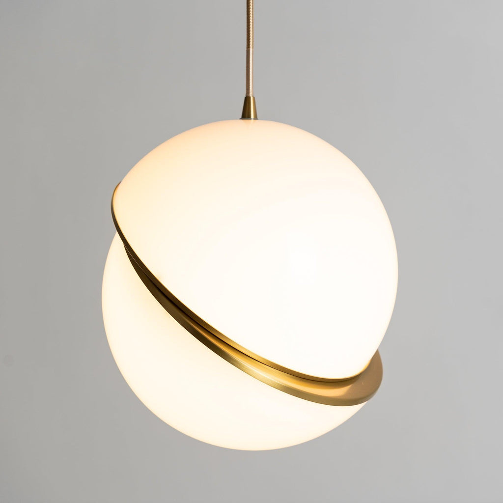 Lit warmly from within, this Clérachic pendant's brass crescent catches the light against a grey wall.