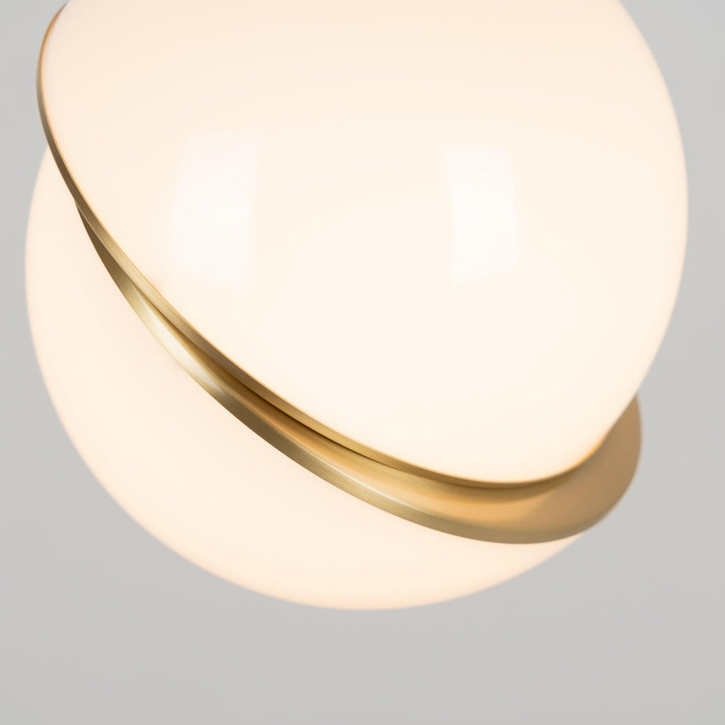 Close view of the glossy opal sphere and brass crescent on this Clérachic pendant, lit from within.