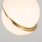 Close view of the glossy opal sphere and brass crescent on this Clérachic pendant, lit from within.