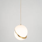 A single Clérachic pendant hangs small in frame on a long brass cord, against a plain grey backdrop.