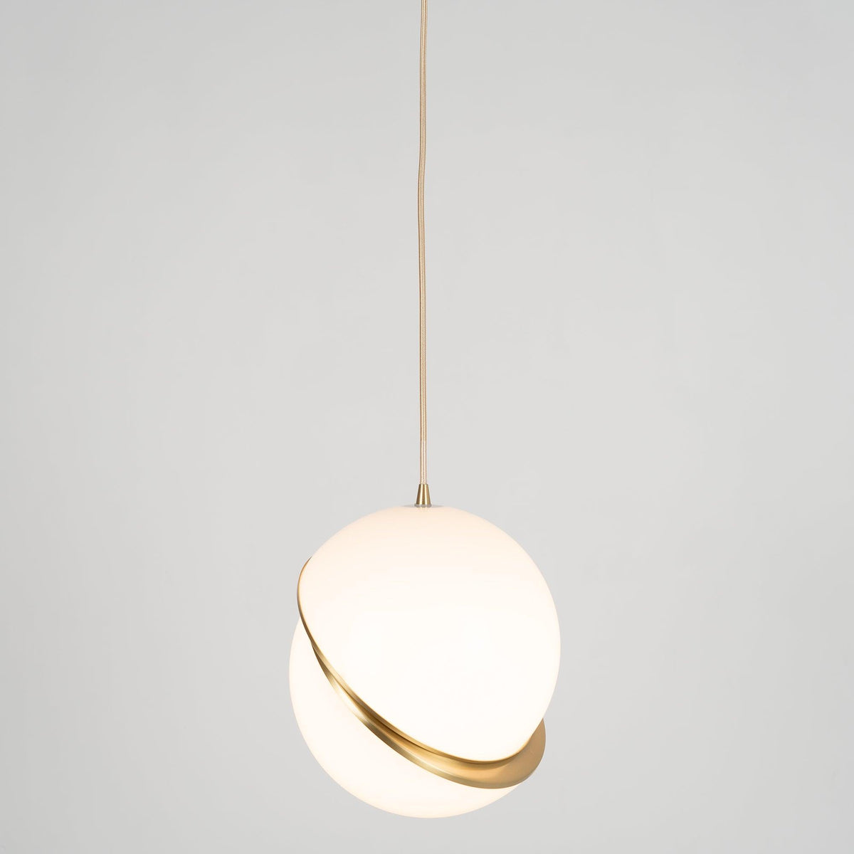 A single Clérachic pendant hangs small in frame on a long brass cord, against a plain grey backdrop.