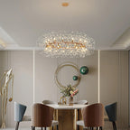 The chandelier lit above a round marble dining table, with velvet chairs and a gold wall hoop behind.