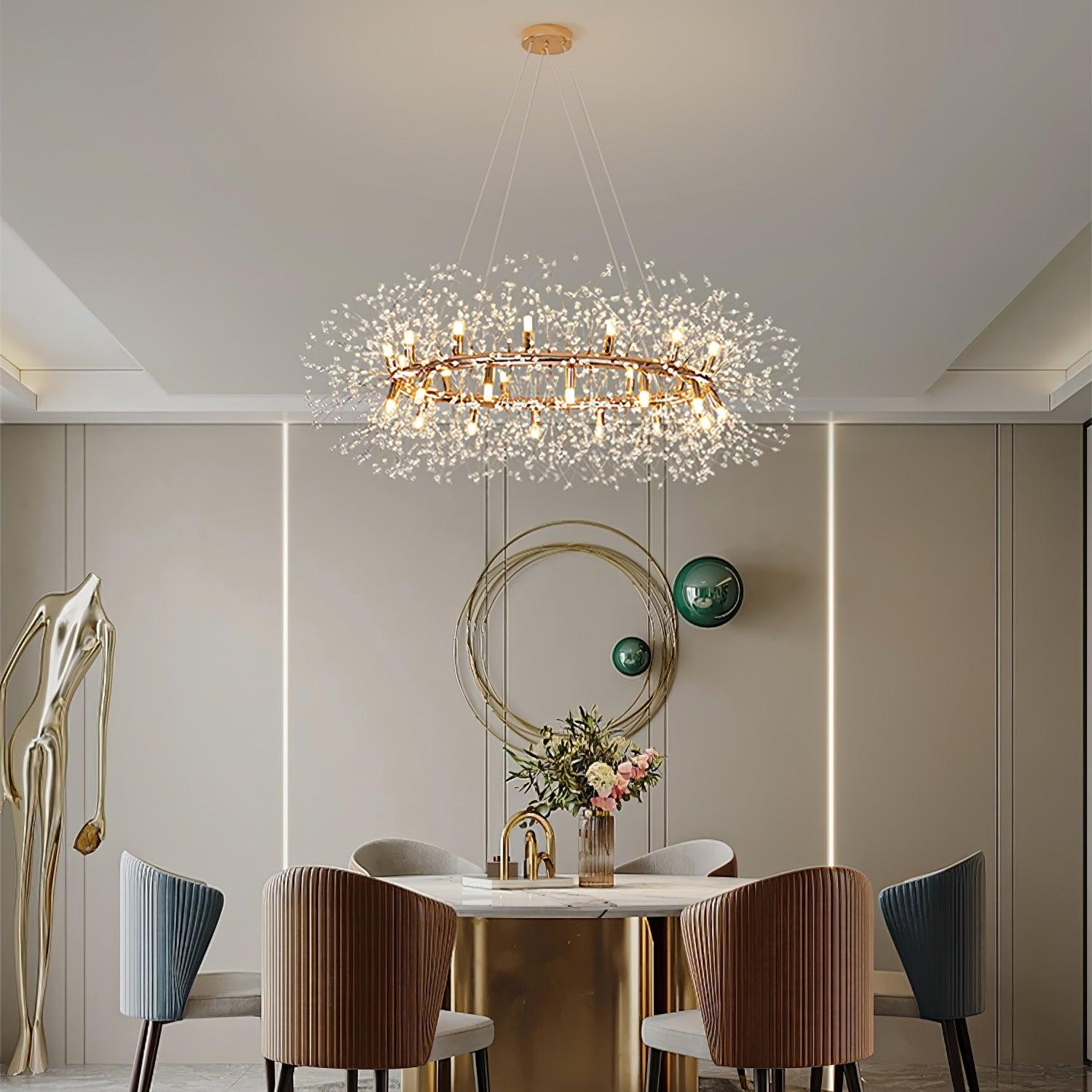 The chandelier lit above a round marble dining table, with velvet chairs and a gold wall hoop behind.