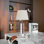 Clérachic's table lamp sits unlit on a marble side table, styled with books, a checkerboard mug and dried flowers.