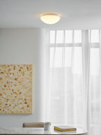 Small and glowing warm, this Clérachic ceiling light lights a room with sheer curtains and a framed painting.